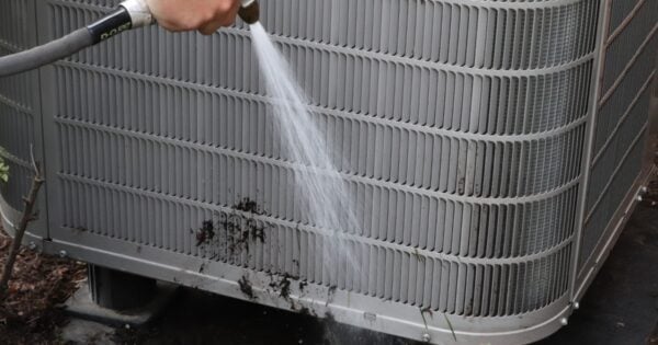 A Henry Heating and Cooling technician is cleaning an air conditioning unit with a hose.