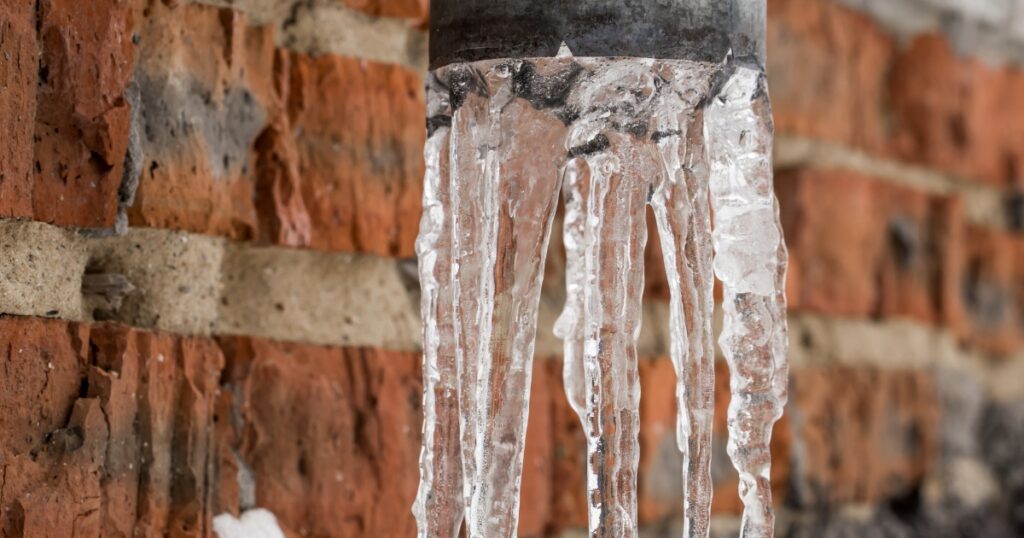 Frozen water sticking out of a pipe outside a brick building.