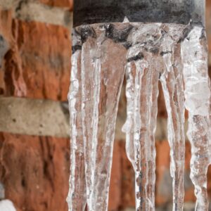 Frozen water sticking out of a pipe outside a brick building.