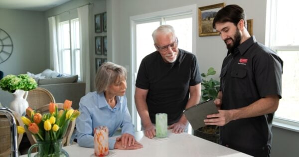 A couple is meeting with an HVAC technician to discuss repairing or replacing their HVAC system.