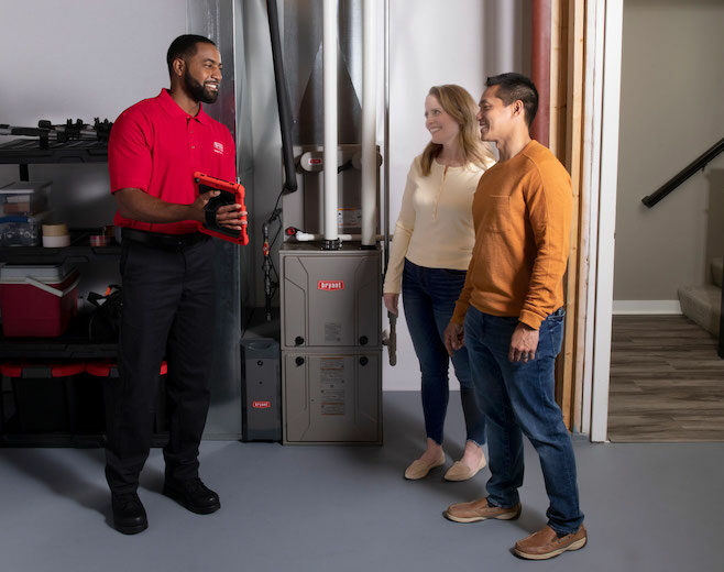 Bryant employee holding a tablet while meeting with two people standing next to a Bryant furnace.